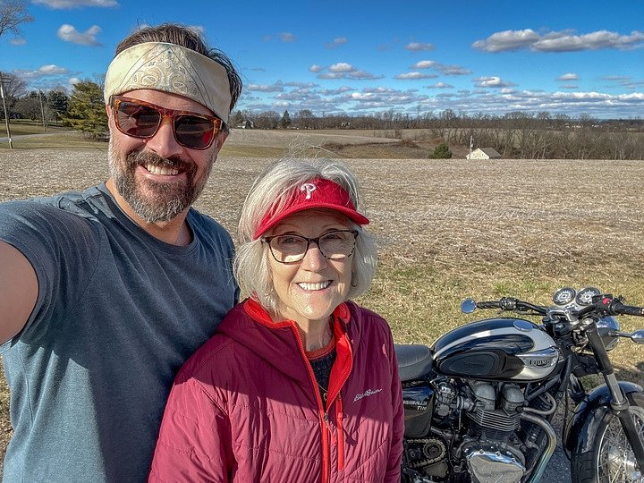 Spurgeon and his mother smiling for a selfie in front of his Triumph Bonneville