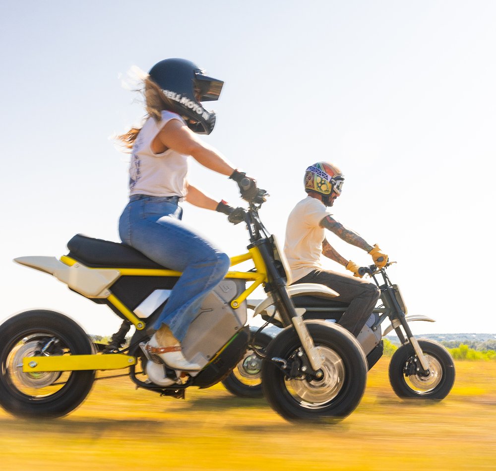 man and a woman riding S4 Honcho small electric motorcycles in a field