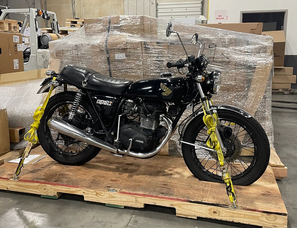 the black Honda CB360T tied down to a wooden pallet and seen inside a warehouse
