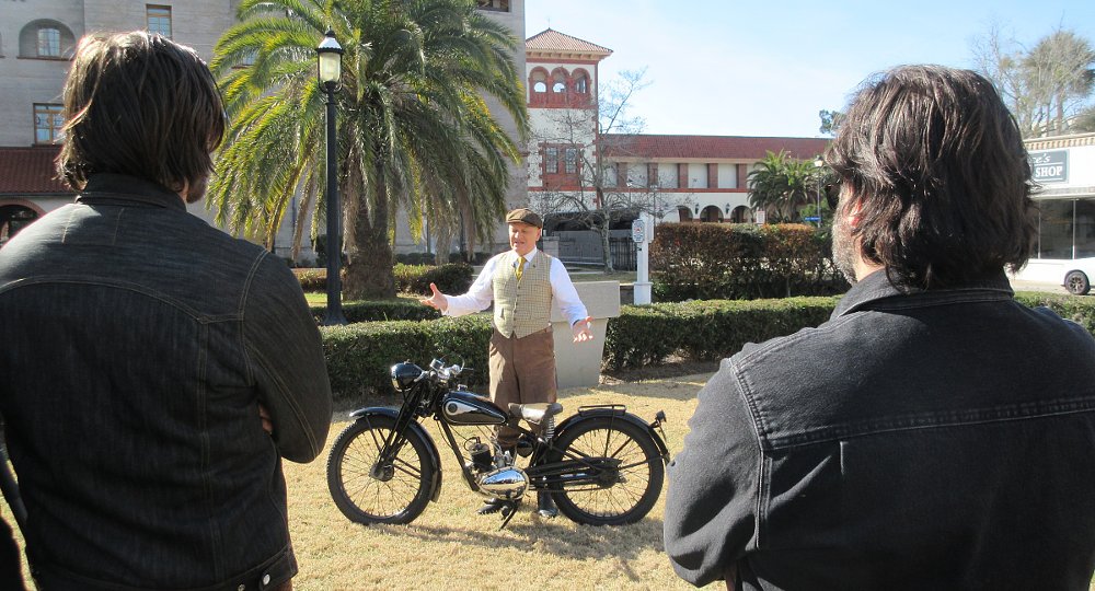 onlookers watching as Gordon May explains the small Flying Flea motorcycle
