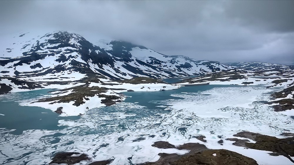 A scenic shot of a snow covered mountain and icy fjord.