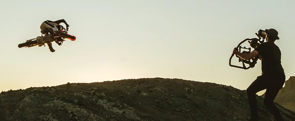 A camera operator films a dirt-bike rider mid-flight.