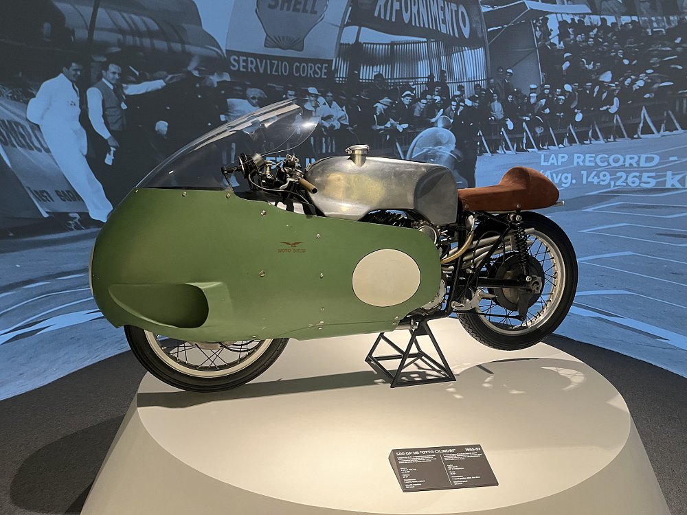 a green and bare-aluminum race bike on a pedestal in the museum