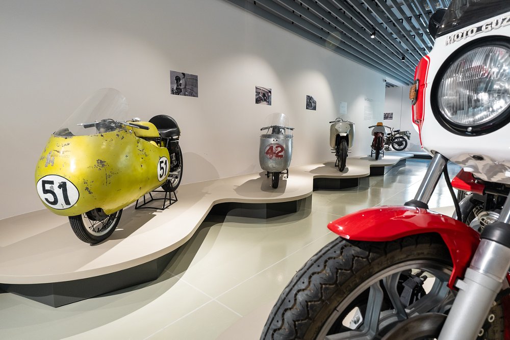 race motorcycles on display on white pedestals against white walls