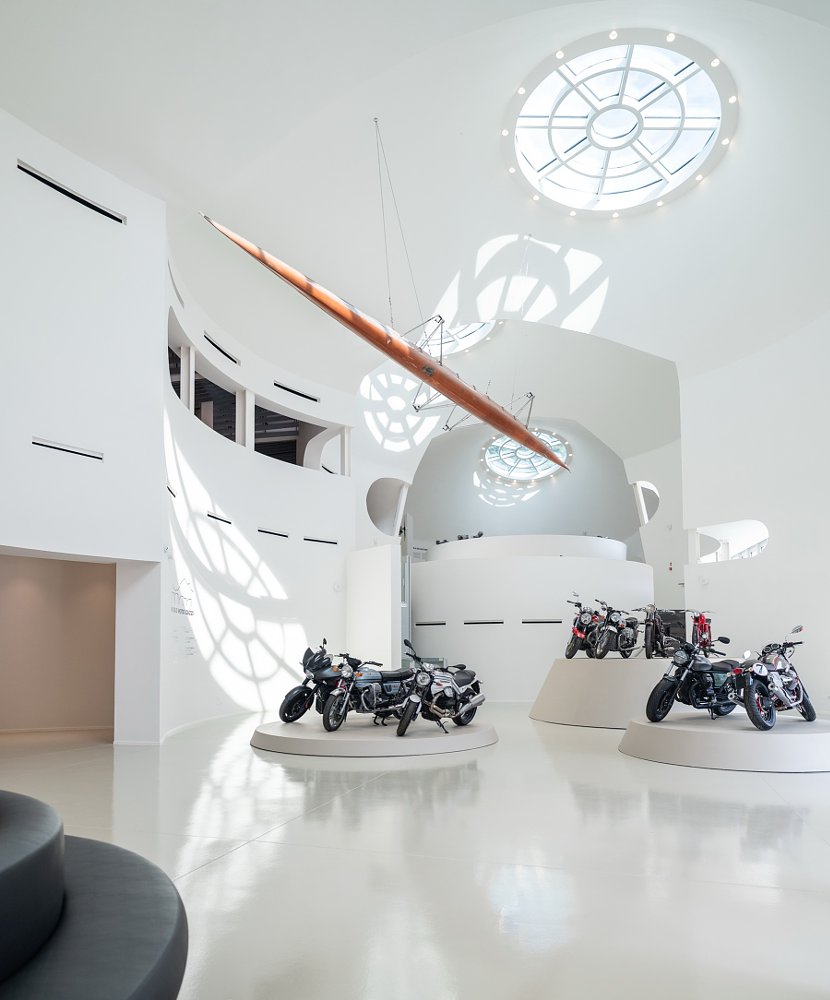 motorcycles on white pedestals against white walls under a skylight in the museum