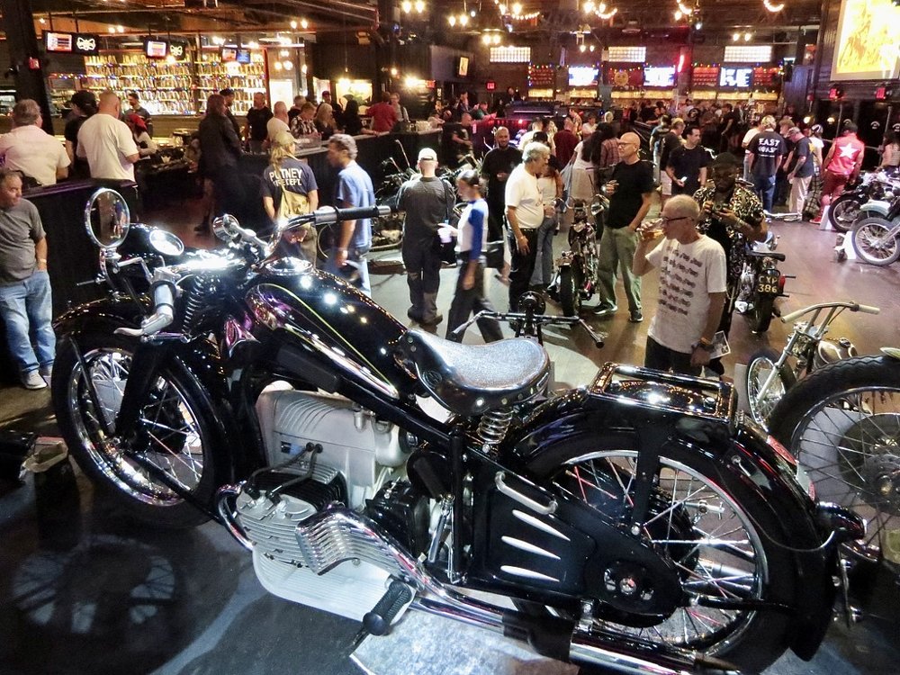 a black Zundapp with an opposed-four-cylinder engine on a pedestal with show attendees in the background