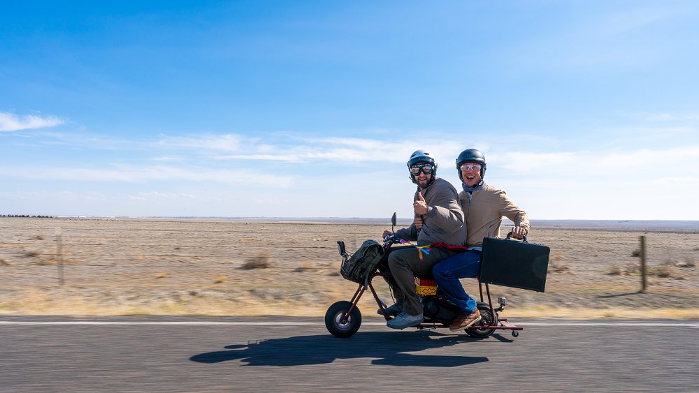 Two men riding a replica of the Dumb and Dumber mini bike.