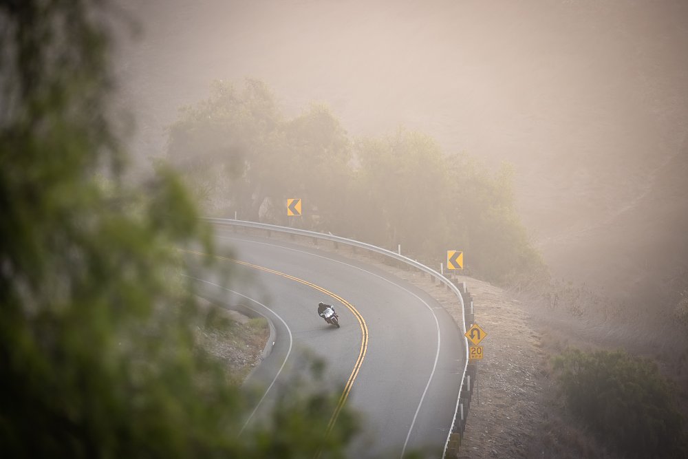 A Honda RC30 rides through a far away corner on a foggy morning.