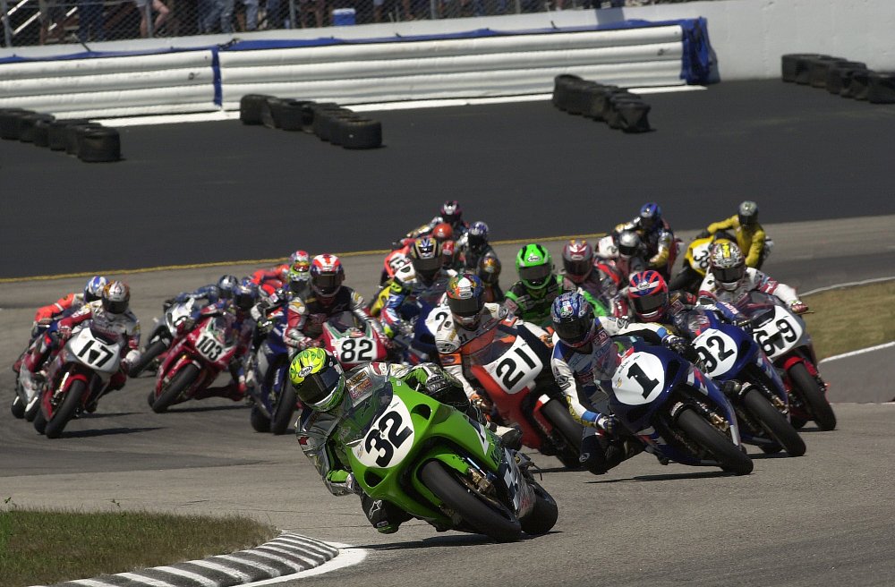 motorcycles in a pack at the start of the AMA Superbike race at New Hampshire Motorcycle Speedway in 2001