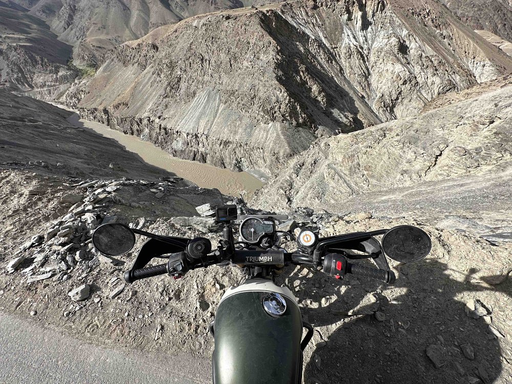 The front of a Triumph Scrambler 400 X stopped just before a cliff leading down to a river.
