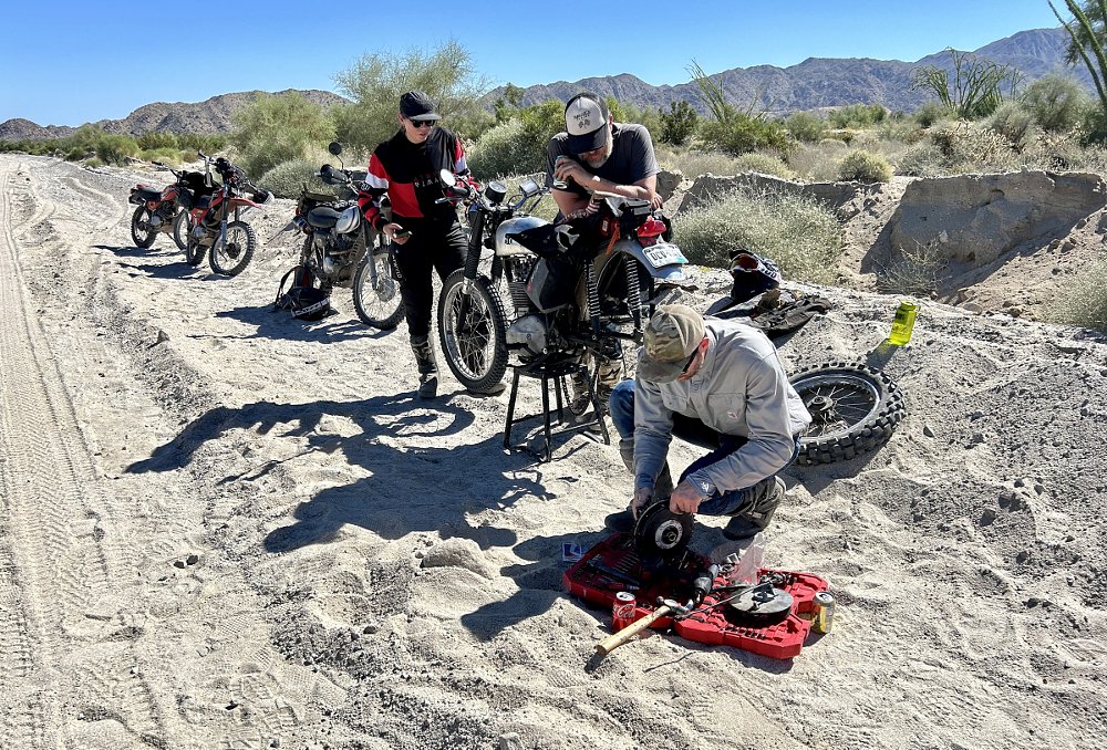 working on the motorcycle alongside a dirt road