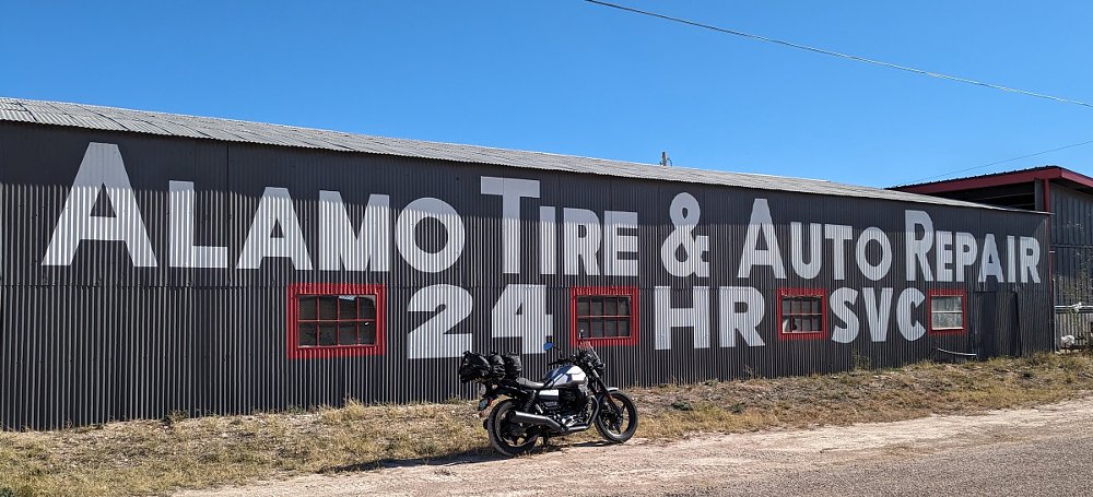 Moto Guzzi parked beside a small town tire repair sign