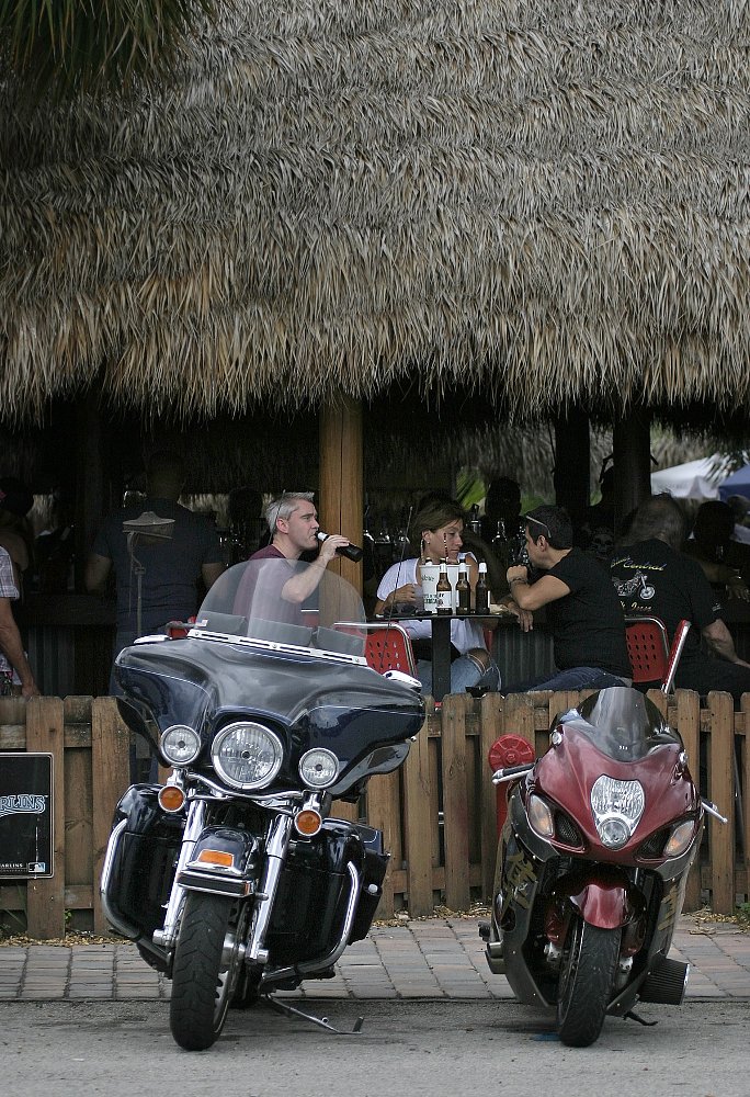riders at an outdoor bar drinking beer with motorcycles parked nearby