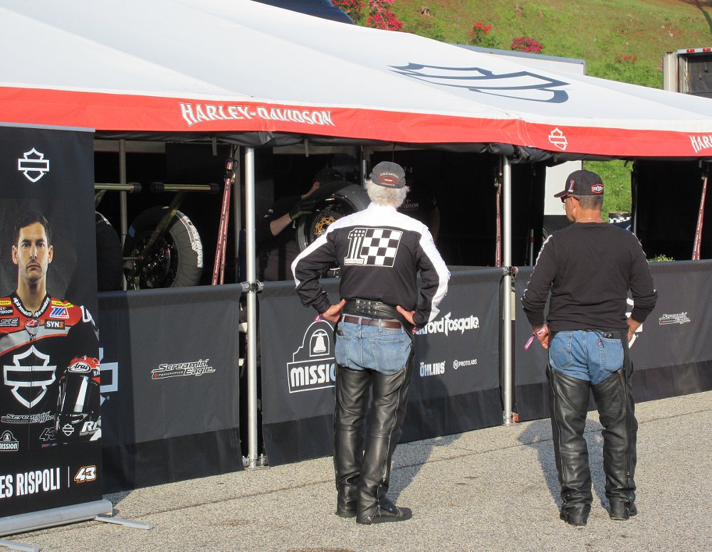 two riders wearing chaps looking at the Harley-Davidson factory race team setup in the paddock