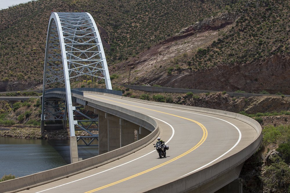rider on a curving desert road and a bridge over a river