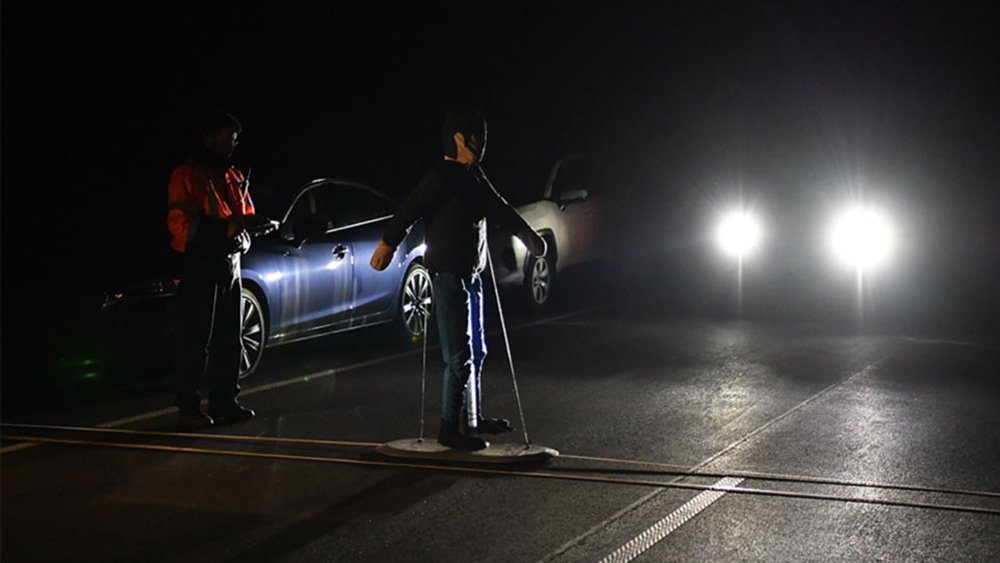 During a nighttime test, a pedestrian dummy crosses the road as a car approaches it.