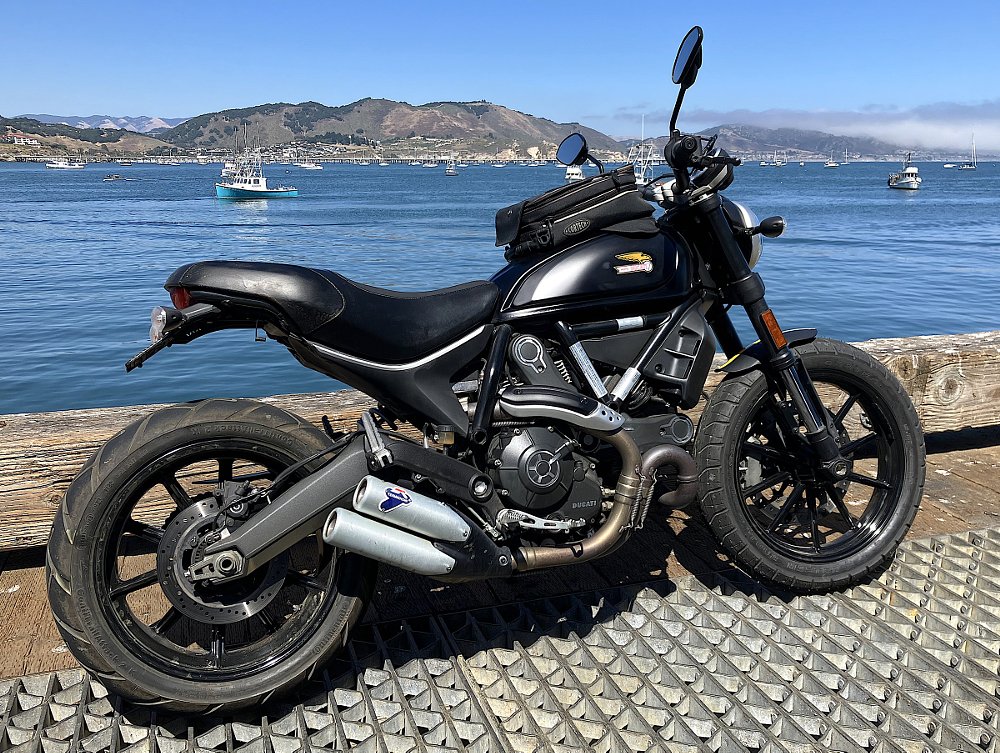 black Scrambler Full Throttle parked in front of a bay with boats on the water