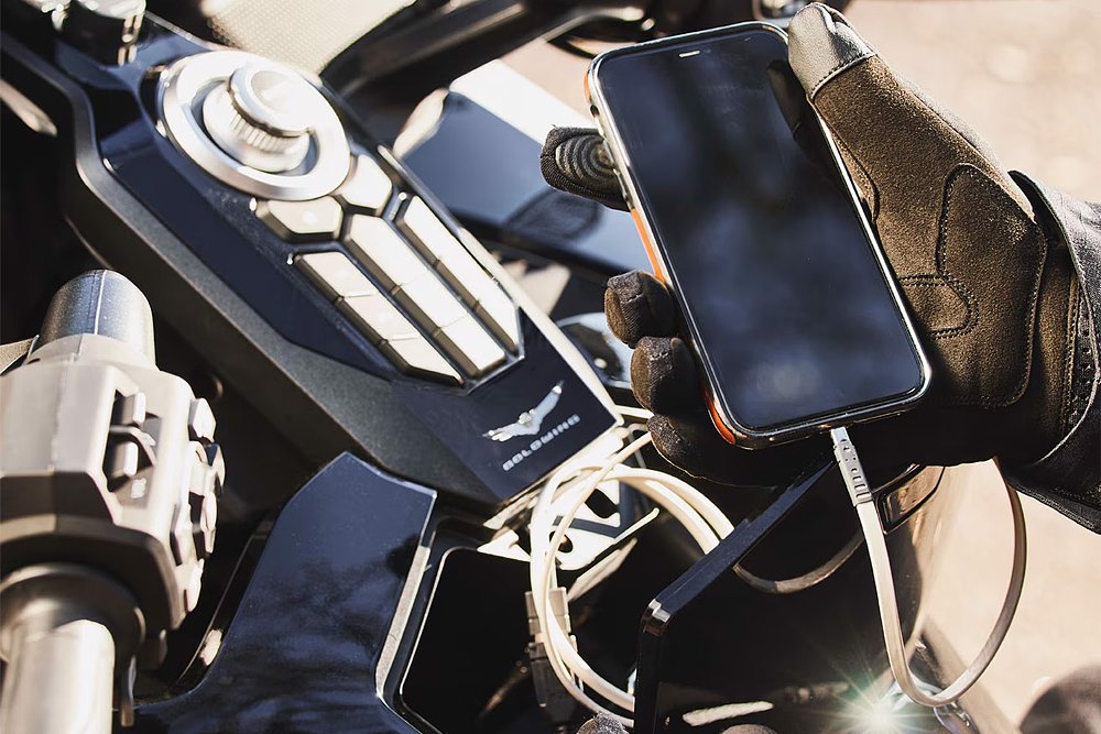 A Honda Gold Wing rider holding a smartphone, which is connected to the bike via a USB cable.