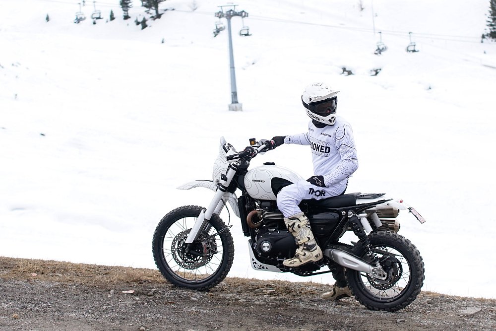 white custom Triumph with a rider dressed in white on a road lined by snow