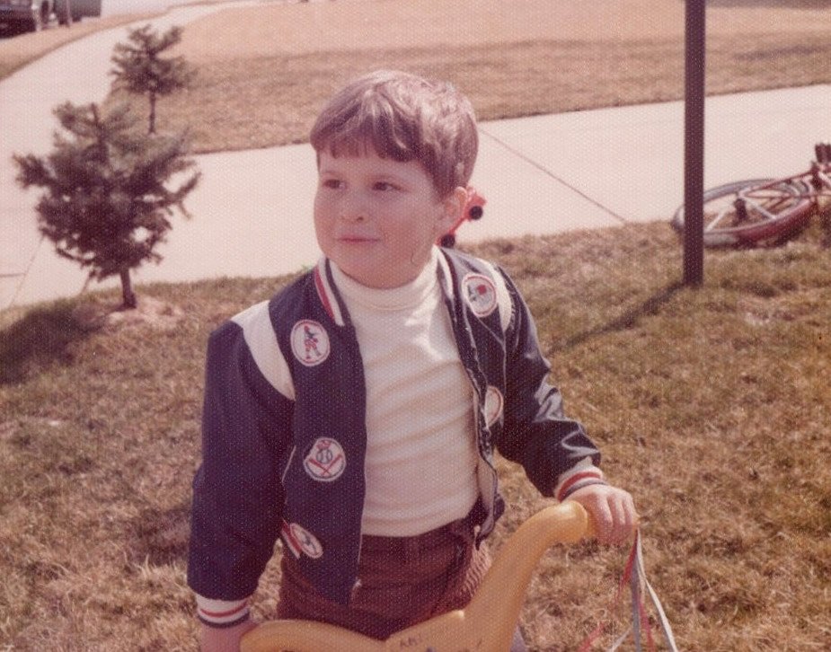 author as a young boy with his Big Wheel in the front yard of a house