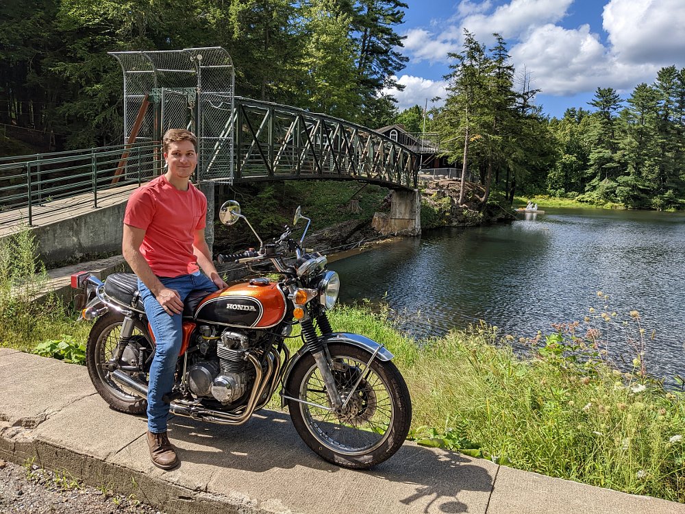 young Leo sitting on his orange CB500 in front of a lake and dam