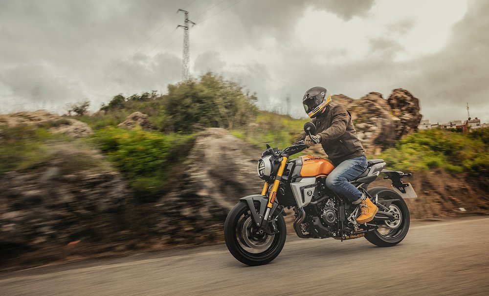 rider on a gold-colored GSX-8T on a road with rocky vegetation in the background