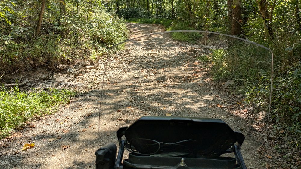rider's view of the trail ahead behind the Canyon's windscreen, showing a dry creek bed
