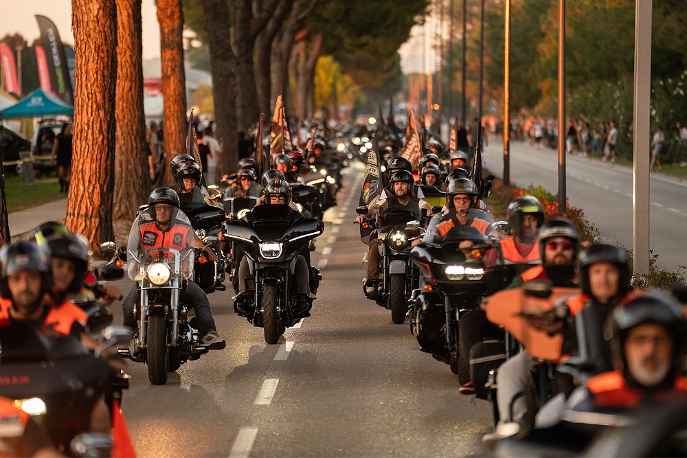 Endless rows of Harley-Davidson baggers ride down a Lignano Sabbiadoro street during sunset.