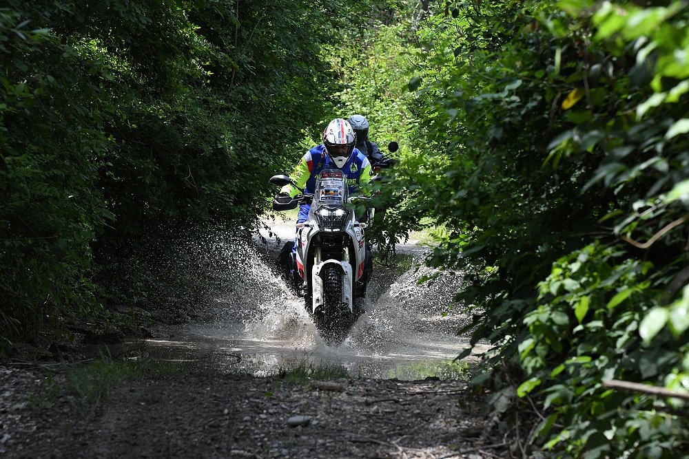 An ADV rider fords through a stream cutting across an off-road trail.